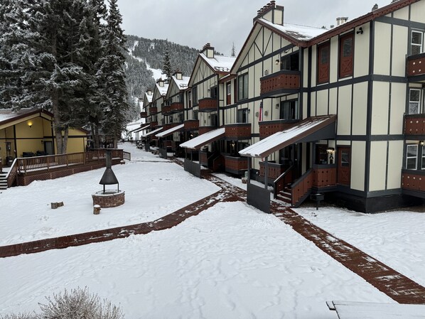 A snow-covered street with traditional buildings, a wooden walkway, and a bench.