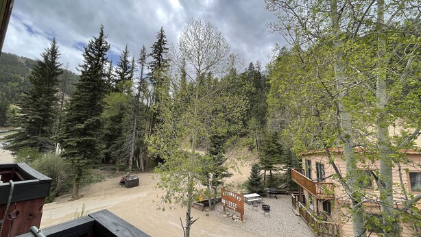 A view of a lodge with a gravel driveway, surrounded by trees and a mountainous backdrop. - Auslander Condominiums (Red River)