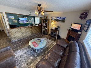 A living room with a brown leather sofa, a coffee table with magazines, a fireplace, and a television.