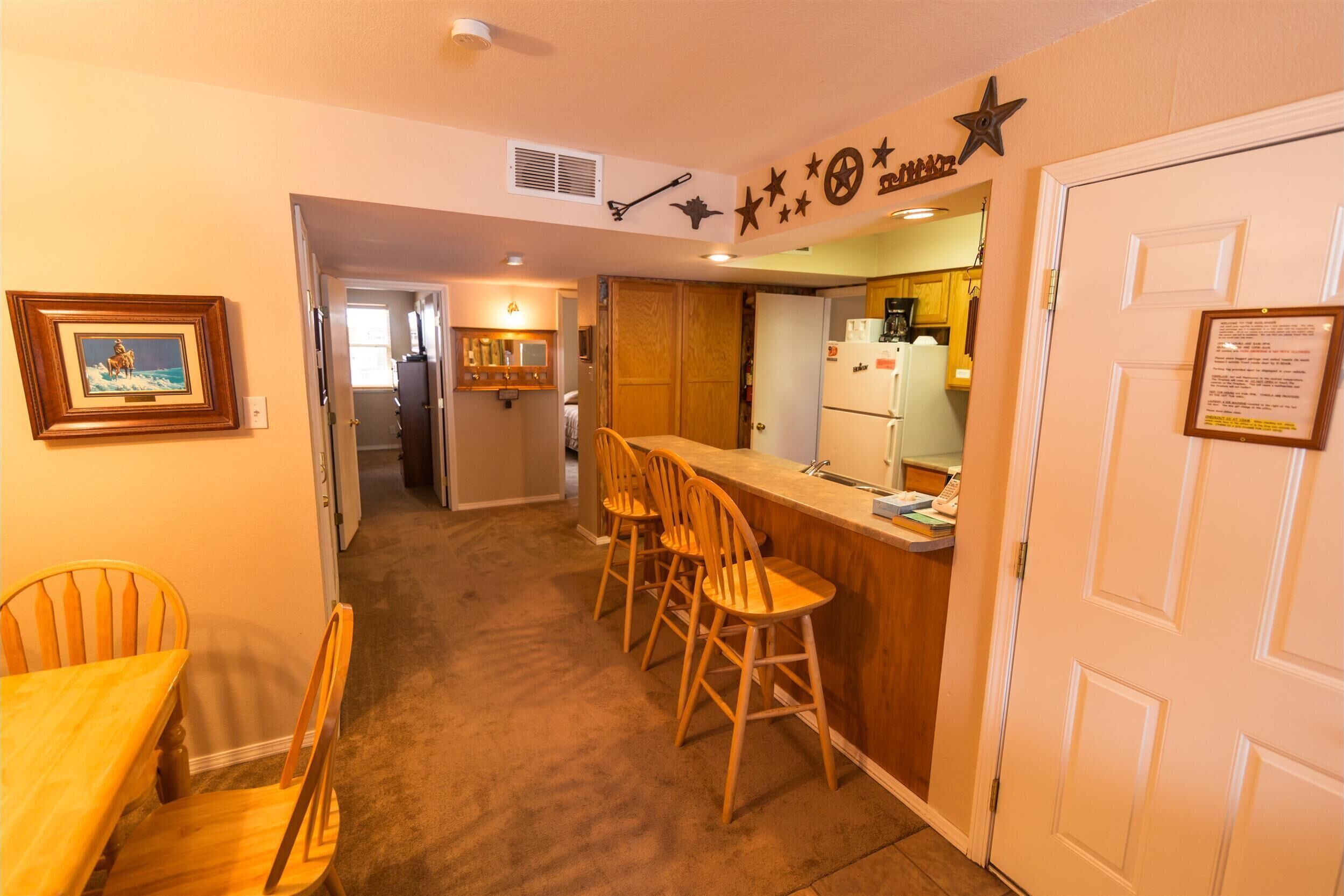 A compact kitchen with a wooden bar counter, a dining area with a table and chairs, and a refrigerator.