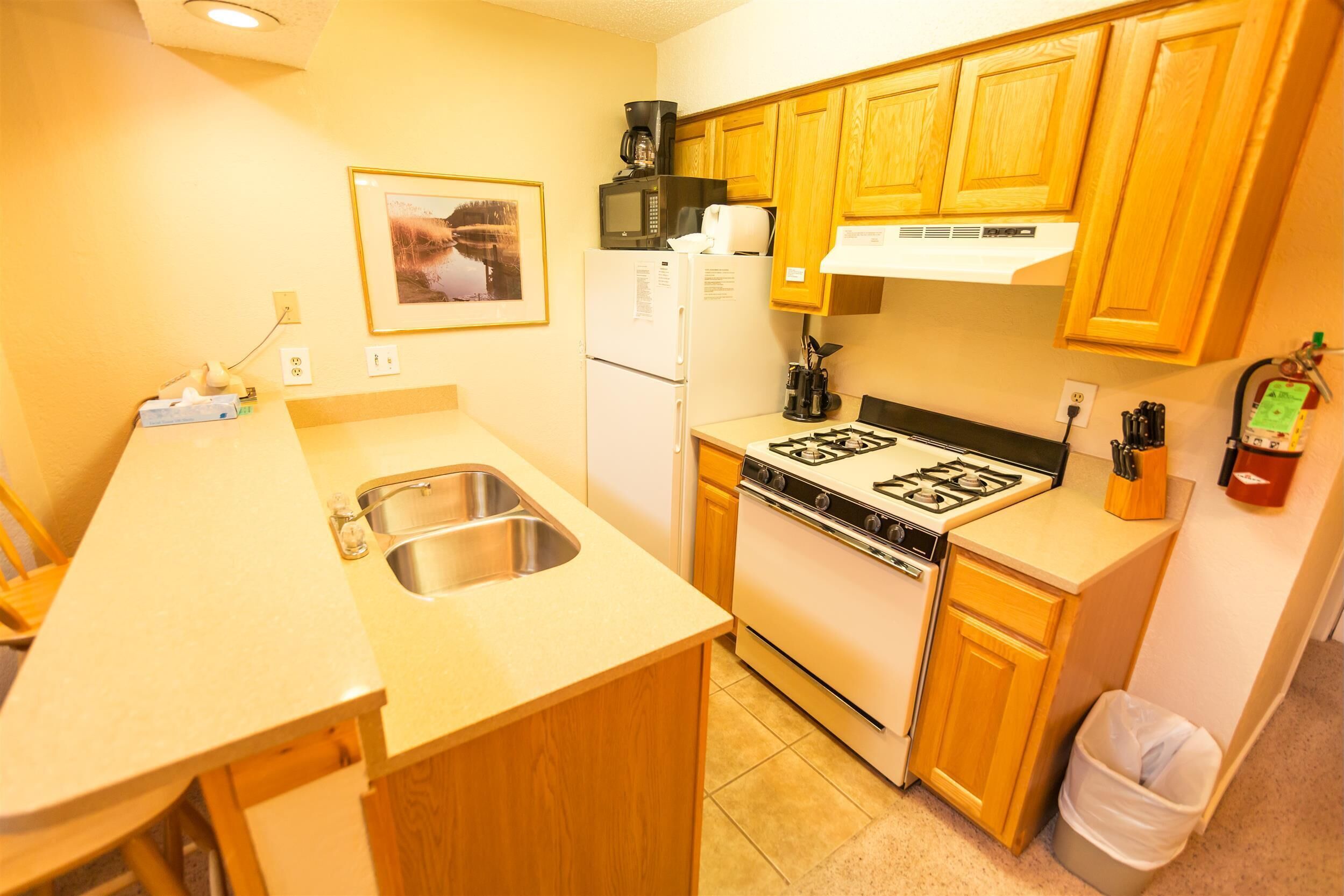 A compact kitchen with wooden cabinets, a stainless steel sink, a stove, and a refrigerator.