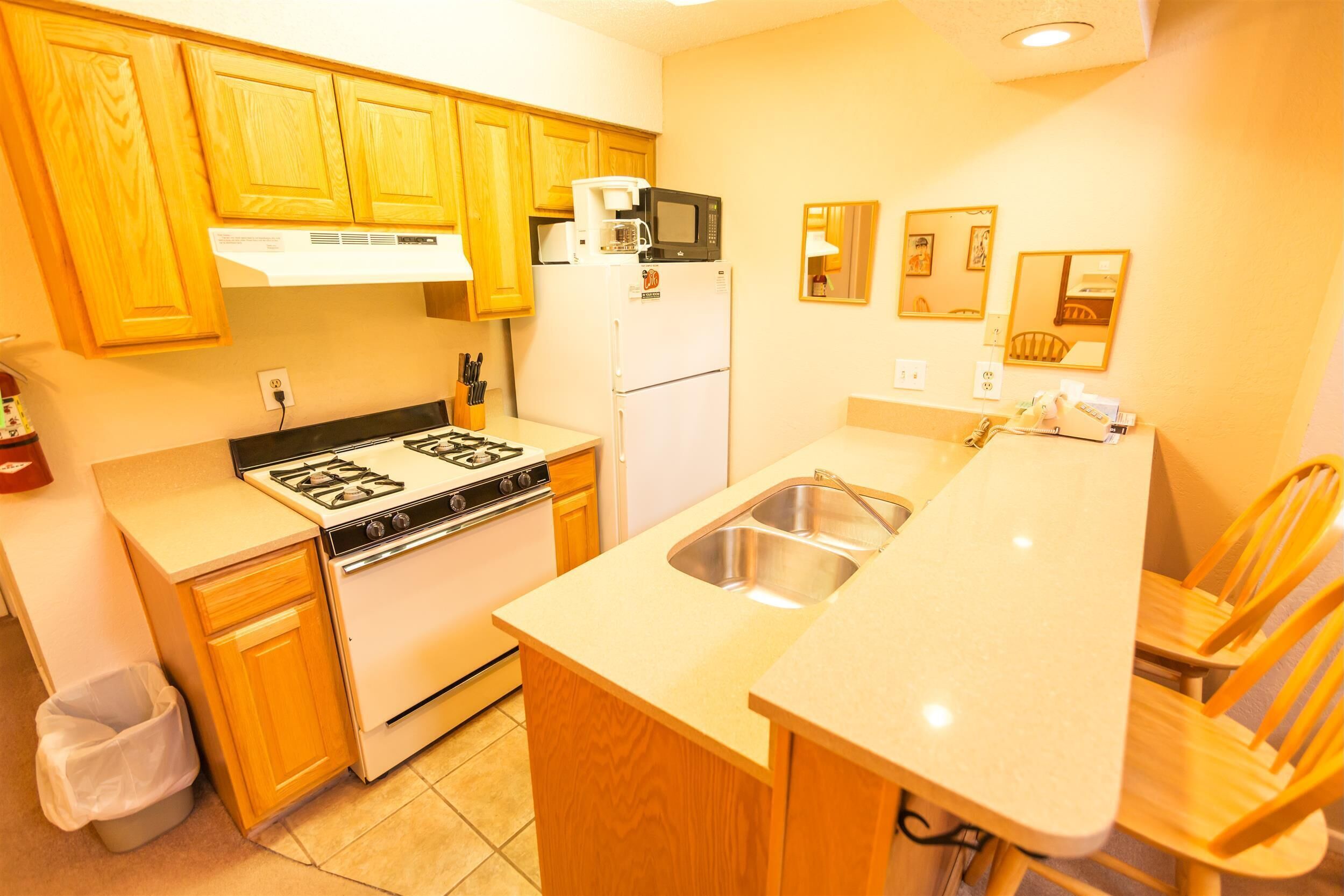 A compact kitchen with wooden cabinets, a stove, a microwave, and a sink.
