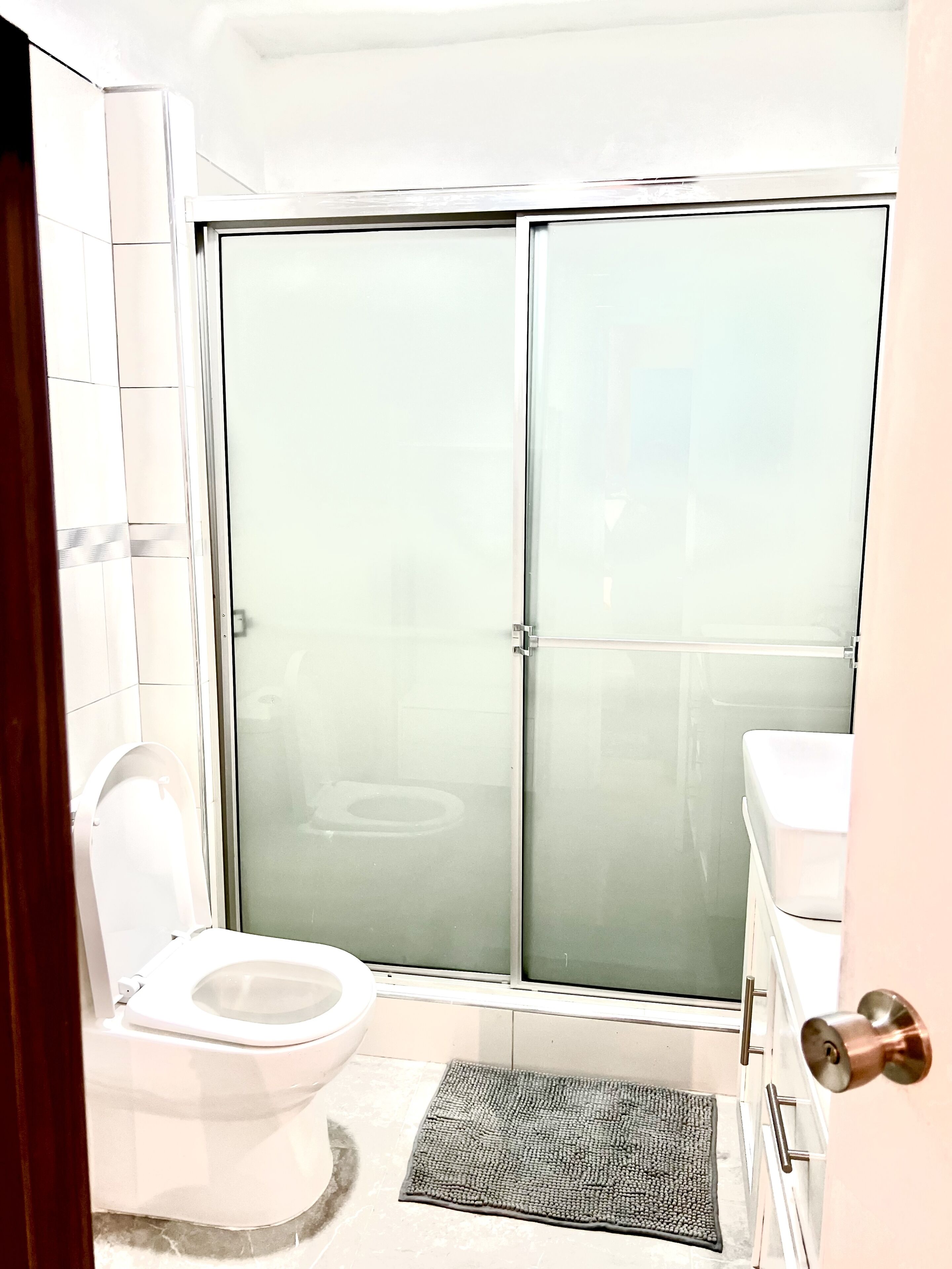A bathroom with a toilet, a shower with frosted glass doors, a sink, and a towel rack.