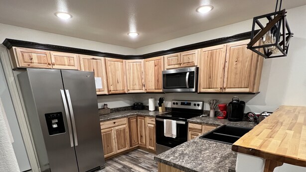 A modern kitchen with wooden cabinets, stainless steel appliances, a granite countertop, and a black trash bin. - New cute clean 4plex w/game rm, centrally located between North Pole & Fairbanks (Fairbanks)