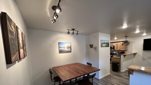 A dining area with a wooden table and chairs, a ceiling light fixture, and artwork on the walls. - New cute clean 4plex w/game rm, centrally located between North Pole & Fairbanks (Fairbanks)