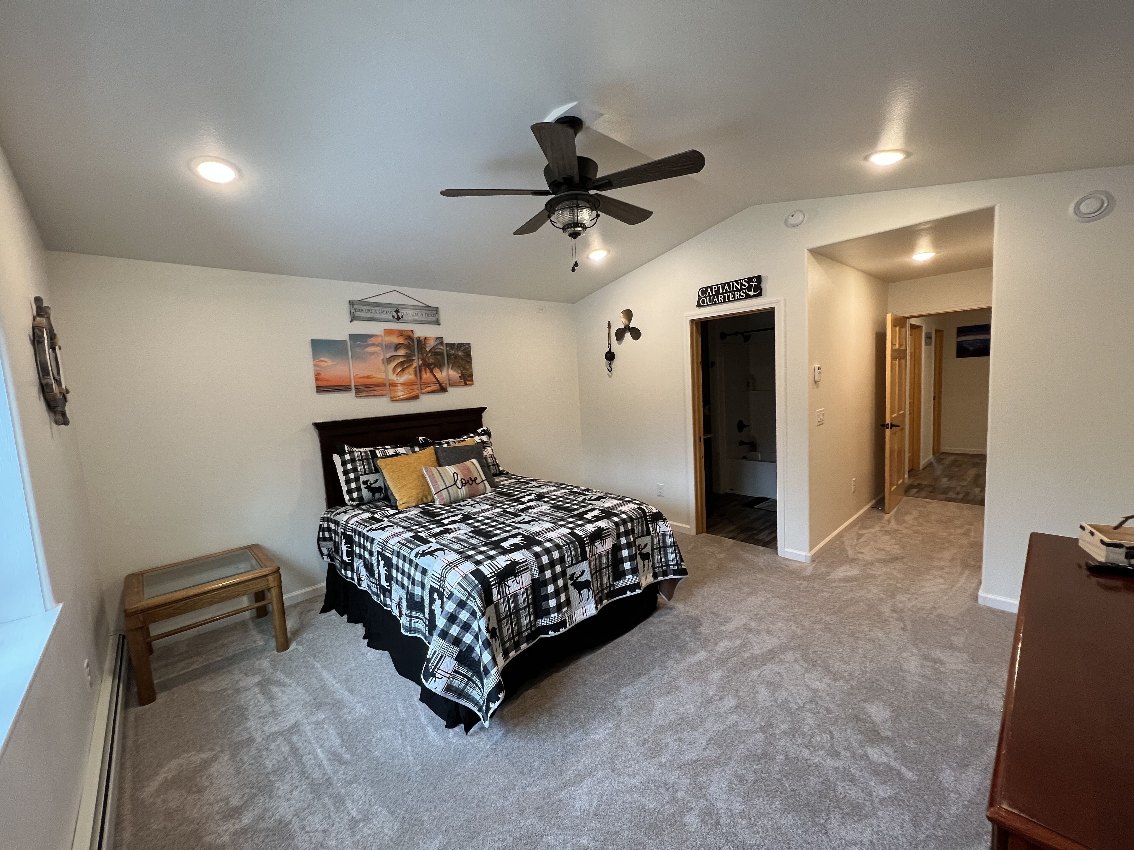 A bedroom with a bed, a ceiling fan, a door labeled 'Captain's Quarters,' and a small bench.