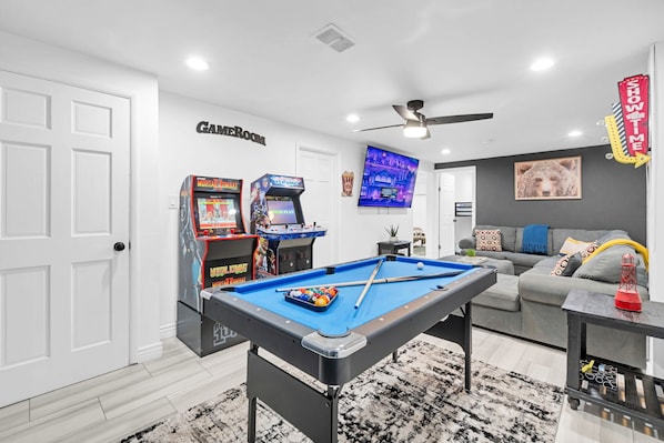 Une pièce équipée d’une table de billard, de jeux d’arcade, d’un canapé et d’un téléviseur.