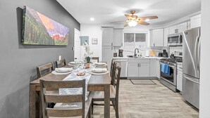 A modern kitchen with white cabinets, a stainless steel refrigerator, and a ceiling fan.