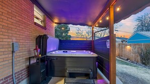 A hot tub in a covered outdoor area with a brick wall, a wooden fence, and a view of the sunset.