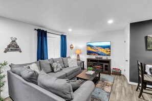 Un salon moderne avec un canapé gris, une table basse, un téléviseur et une cheminée.