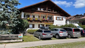 A two-story wooden building with balconies, parked cars, and a clear blue sky.