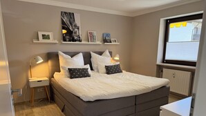A neatly arranged bedroom with a large bed, bedside lamps, a radiator, and framed pictures on the wall.