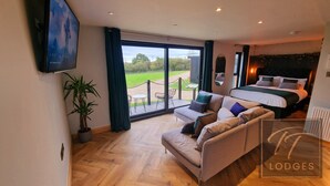 A modern bedroom with a large bed, a sofa, and a TV. There is a balcony with a view of the outdoors. - TT Lodges (Stockton-on-Tees)