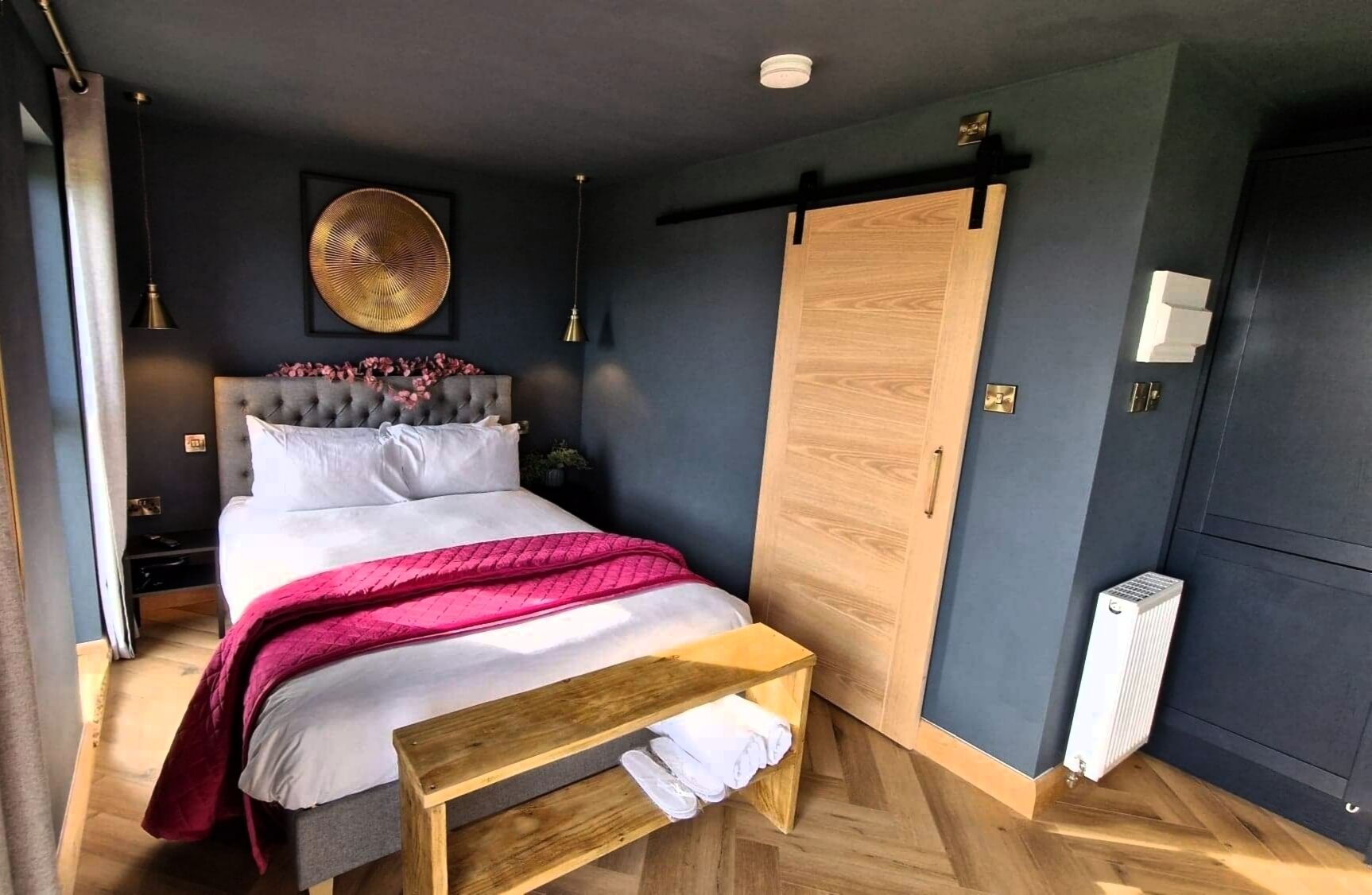 Un dormitorio moderno con una cama grande, un banco de madera, un armario y un radiador.