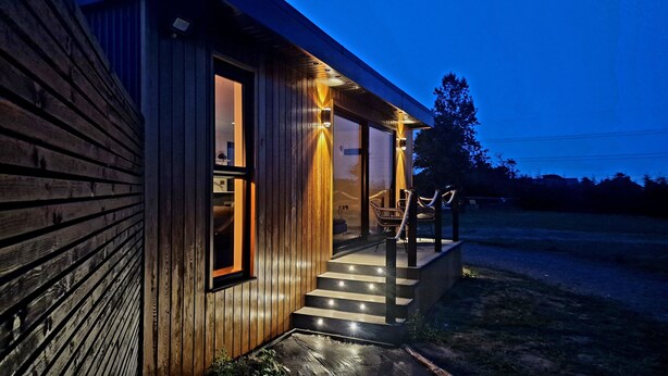 A wooden cabin with a porch, steps leading to a door, and a chair outside. - TT Lodges (Stockton-on-Tees)