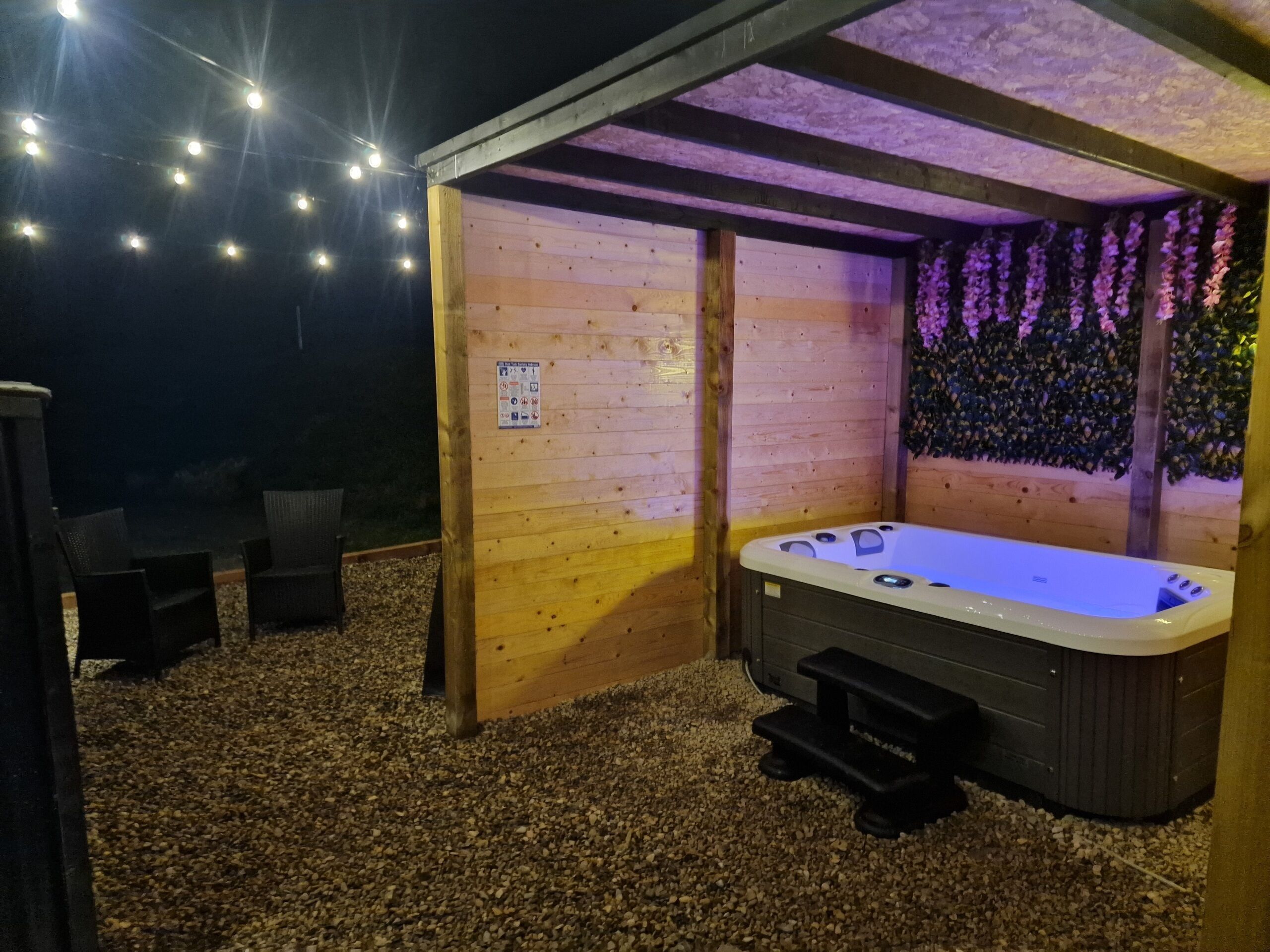 An outdoor hot tub area with wooden walls, a wooden bench, and string lights.