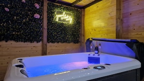 A hot tub with a neon sign saying "good vibes only" and a wooden wall with a green leafy backdrop. - TT Lodges (Stockton-on-Tees)