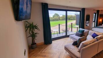 A modern bedroom with a large bed, a sofa, and a TV. There is a balcony with a view of the outdoors.