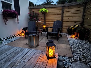 Un patio al aire libre con mesa de madera, dos sillas, un hogar metálico y faroles decorativos.