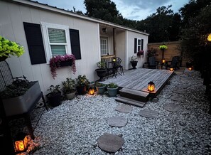 A covered patio area with a wooden deck, potted plants, outdoor furniture, and decorative lighting. - Romantic Escape on Peaceful Mini Farm (Coleman)
