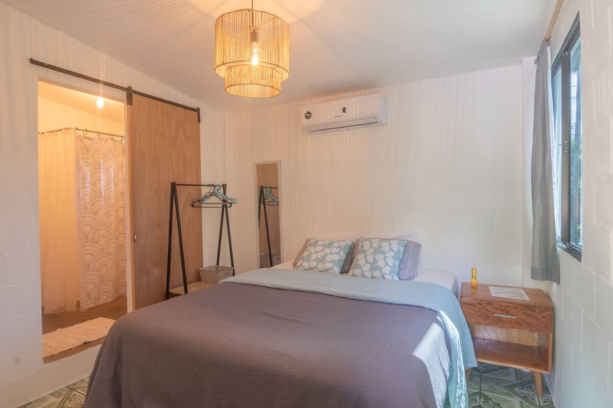 Un dormitorio con cama, lámpara colgante, ventana con cortina y equipo de aire acondicionado.