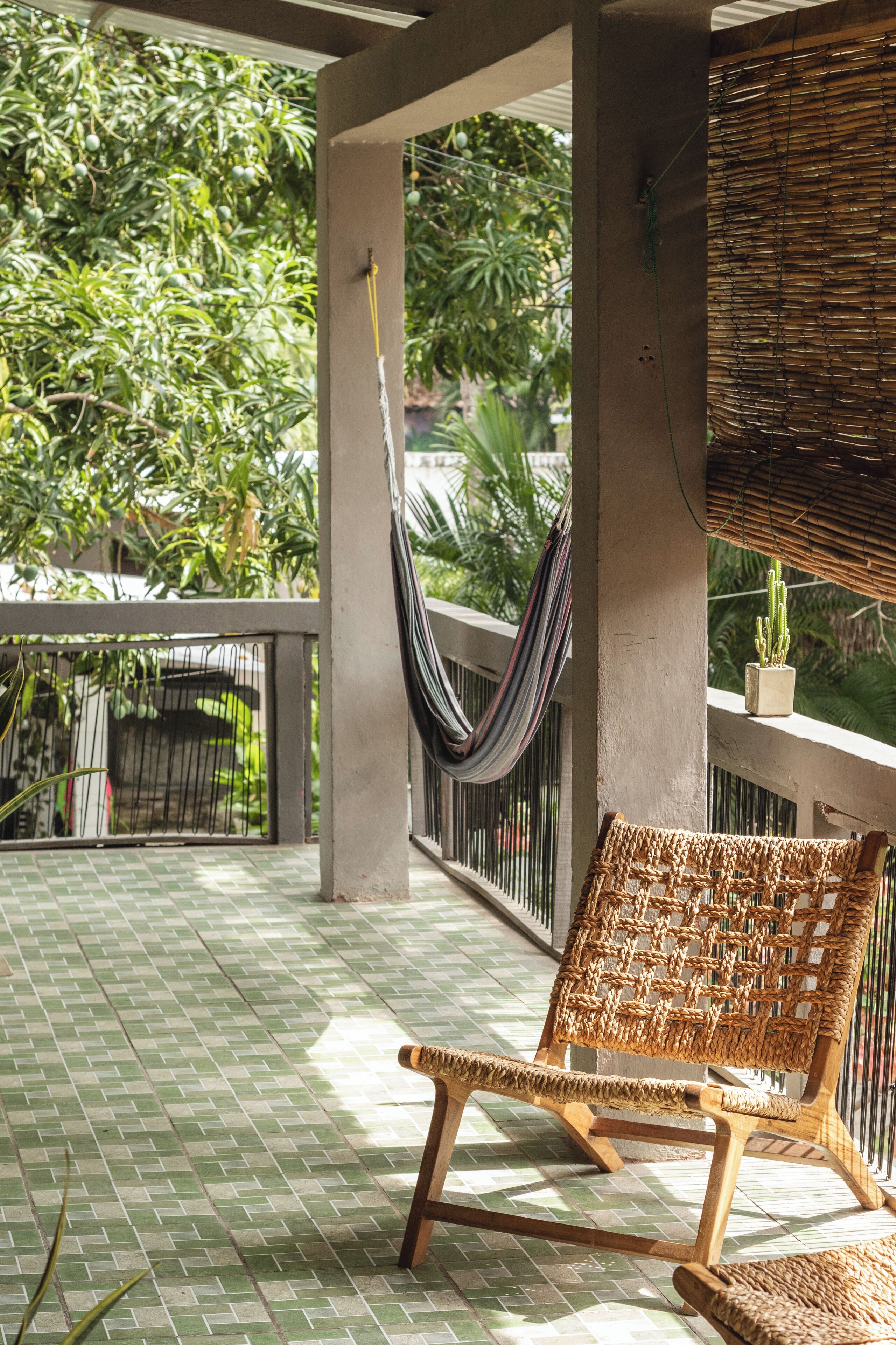 A wicker chair on a tiled balcony with a view of greenery and a hanging hammock.