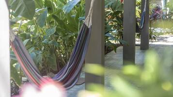 Un hamac est suspendu entre des piliers dans un espace jardin luxuriant, où la végétation est abondante et d’un vert éclatant.