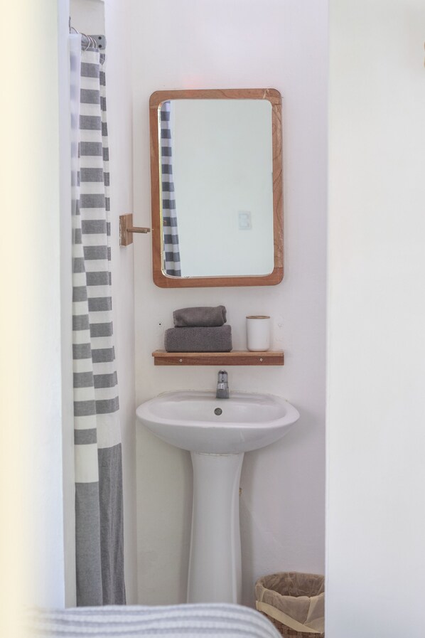 A bathroom with a white sink, a mirror with a wooden frame, a towel rack, and a shower curtain.