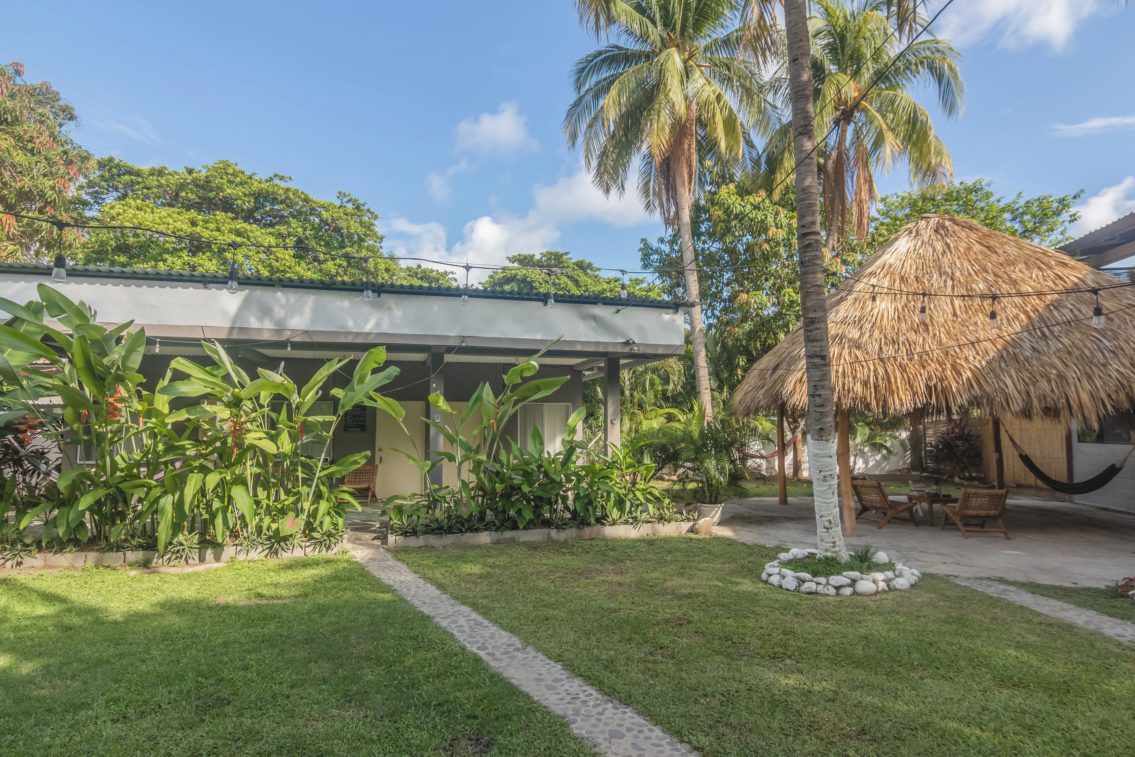 A tropical resort with a thatched-roof hut, palm trees, and a well-maintained lawn.