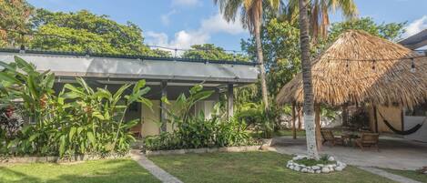 A tropical resort with a thatched-roof hut, palm trees, and a well-maintained lawn.