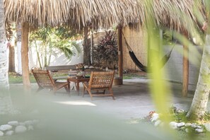 An outdoor dining area with a thatched roof, wooden table, and wicker chairs.