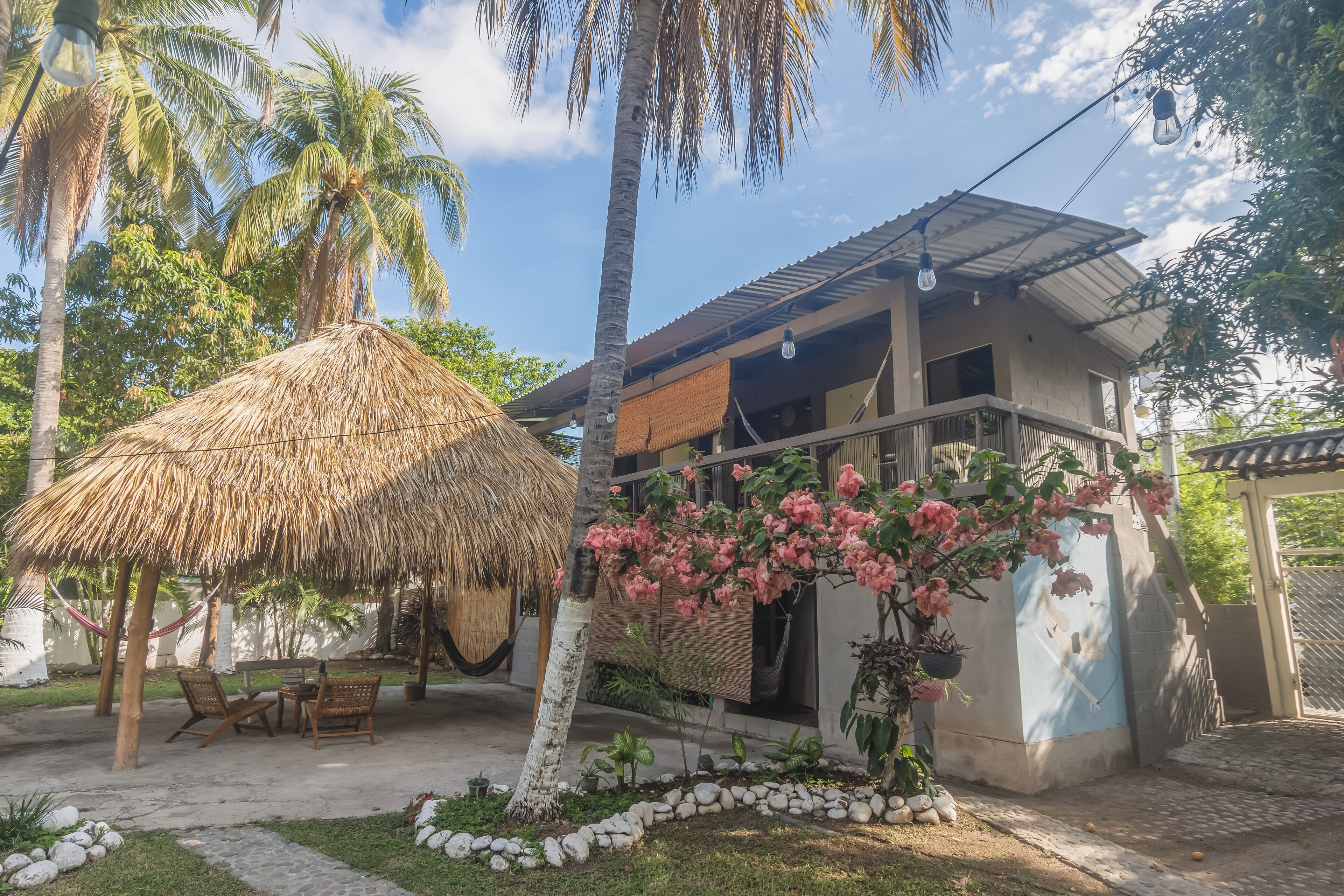 A house with a thatched roof, a balcony, and a garden with pink flowers.