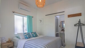 Une chambre à coucher bien rangée, avec un lit, une table de chevet, une fenêtre avec des rideaux, un climatiseur fixé au mur et un luminaire suspendu.