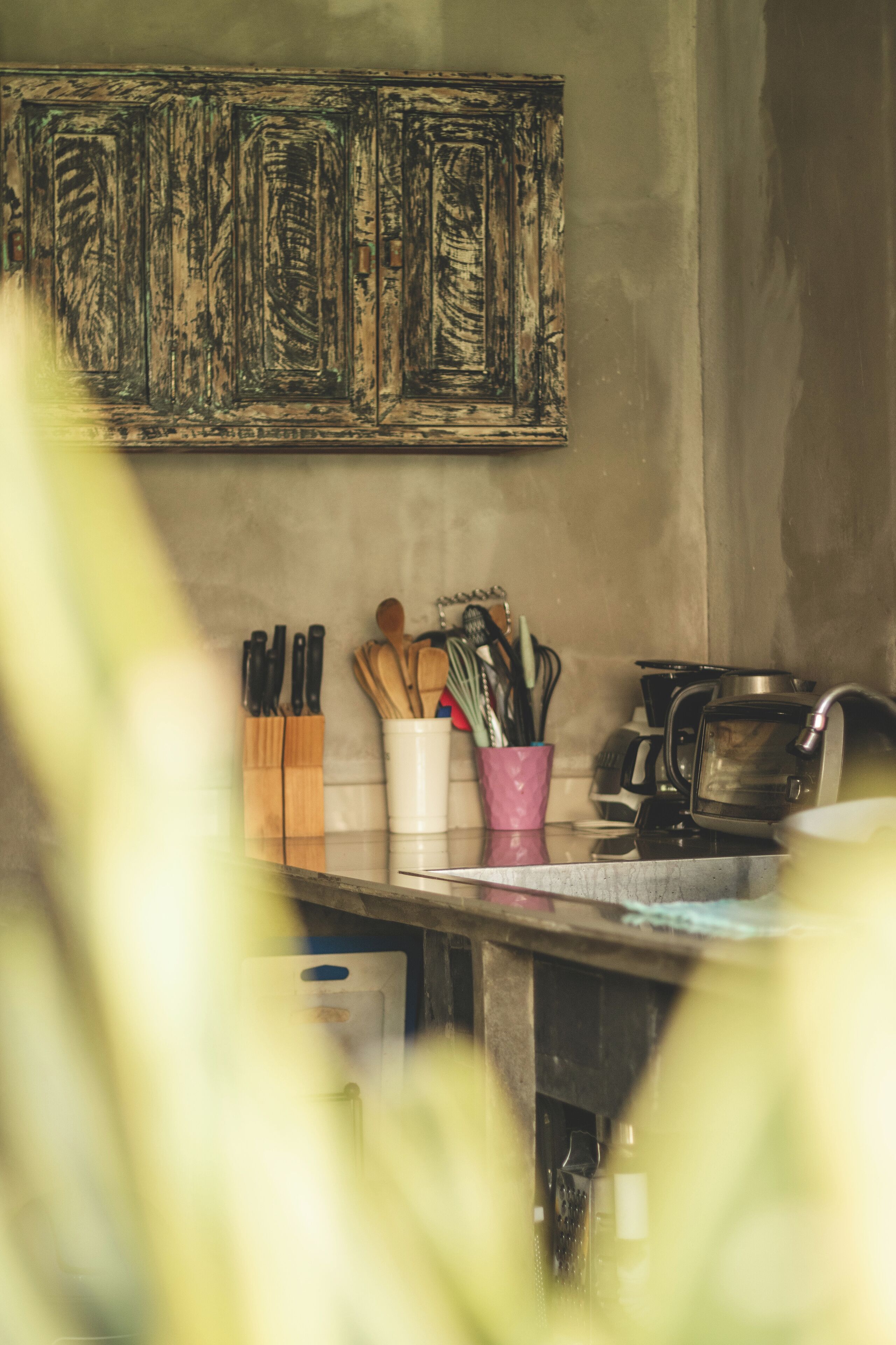 A kitchen with a wooden cabinet, a pink utensil holder, and a coffee maker.