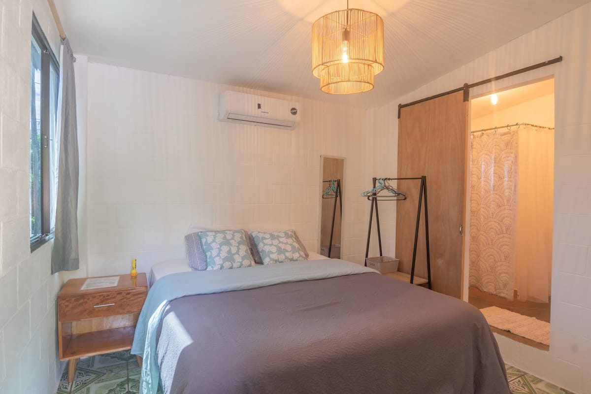 Un dormitorio con cama, mesita de noche, lámpara colgante, armario y zona de ducha.