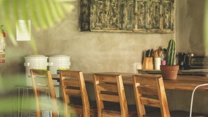Une table à manger en bois, entourée de chaises, avec un cactus en pot et des ustensiles de cuisine en arrière-plan.