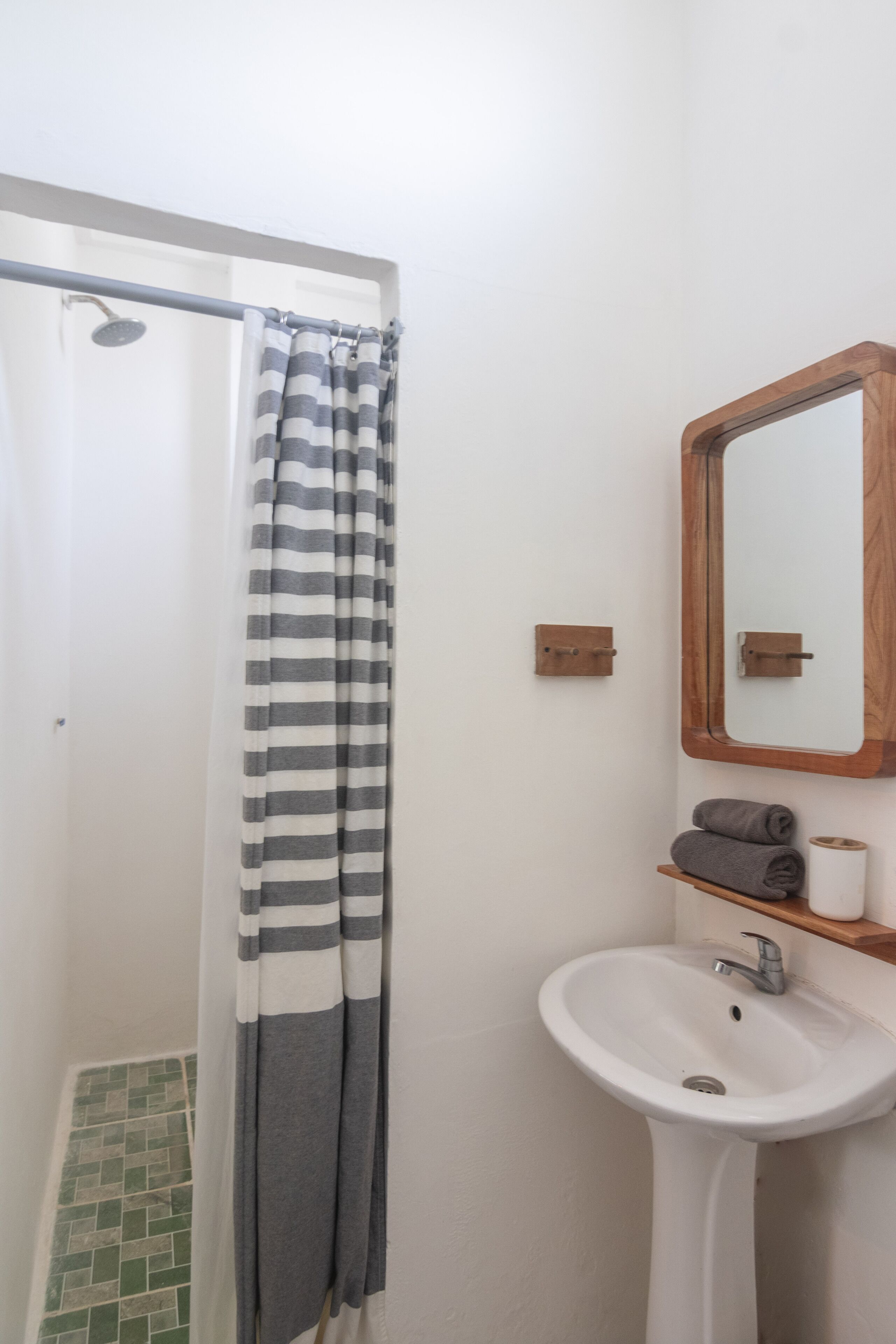 A bathroom with a shower curtain, a sink, a mirror, and a towel rack.
