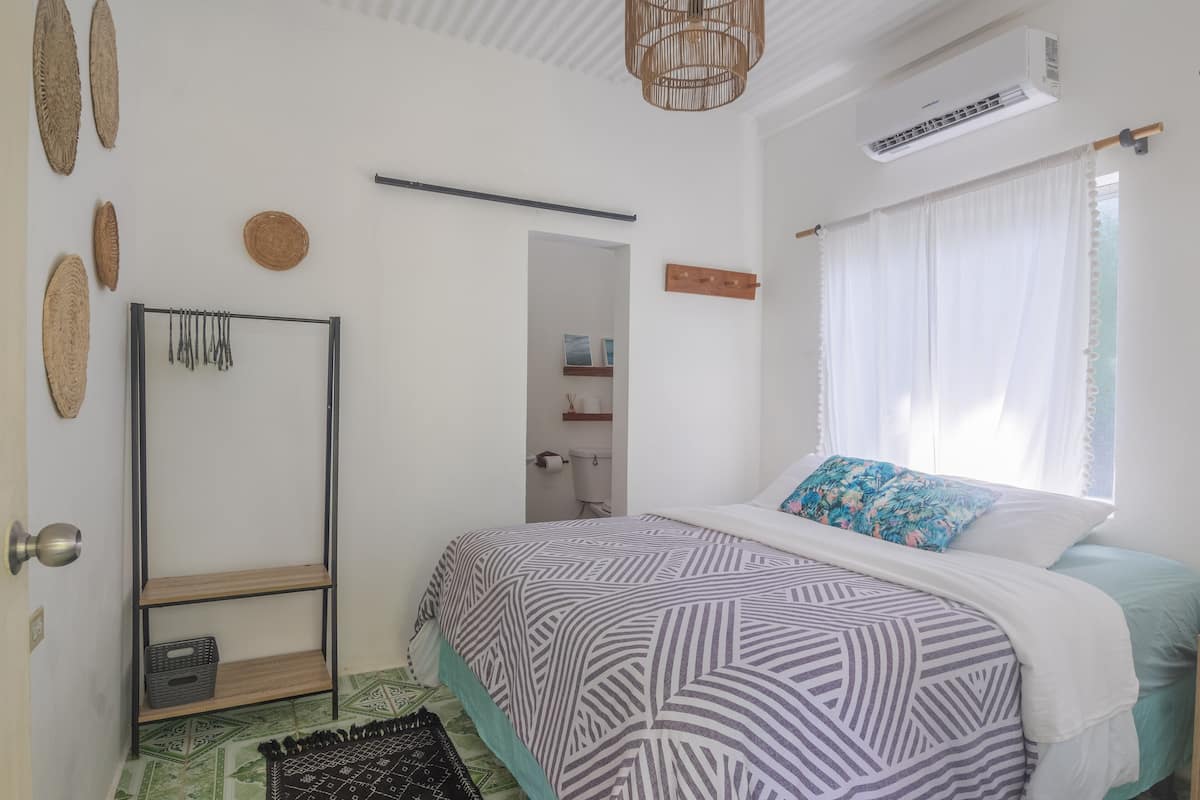 Un dormitorio con cama, armario, estante y ventana con cortinas.