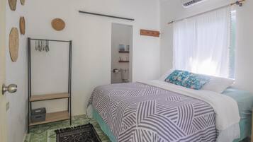 A bedroom with a bed, a wardrobe, a shelf, and a window with curtains.