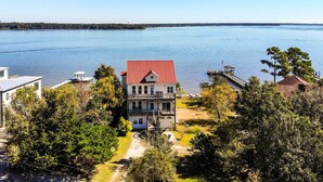 Una casa de dos pisos con techo rojo, rodeada de árboles y vista al lago.