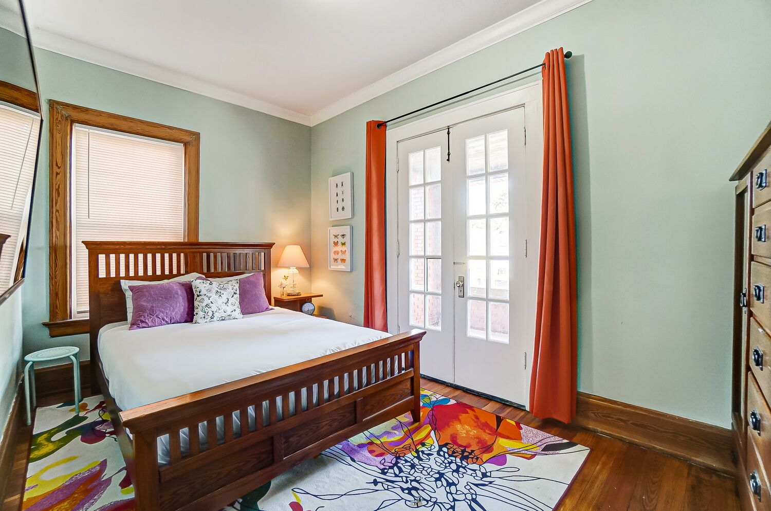 A bedroom with a wooden bed, a nightstand, a colorful rug, and a door with a view.