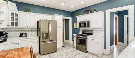Una cocina moderna con armarios blancos, electrodomésticos de acero inoxidable y baldosas de piso estampadas.