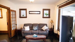 A living room with a sofa, a coffee table, a television, and a door. - Charming historic home w/ parking, walk to downtown, waterfront, shops & more. (North Bay)