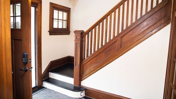 A wooden staircase with a handrail, a door with a black handle, and a patterned floor. - Charming historic home w/ parking, walk to downtown, waterfront, shops & more. (North Bay)