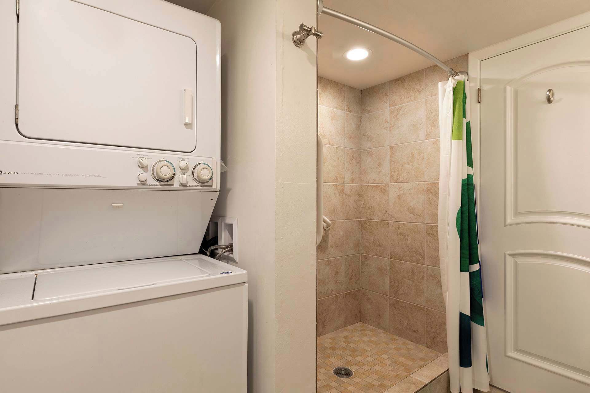 Une salle de bain compacte équipée d’un lave-linge et d’un sèche-linge intégrés, d’une cabine de douche avec rideau et d’une porte dotée d’un porte-serviettes.