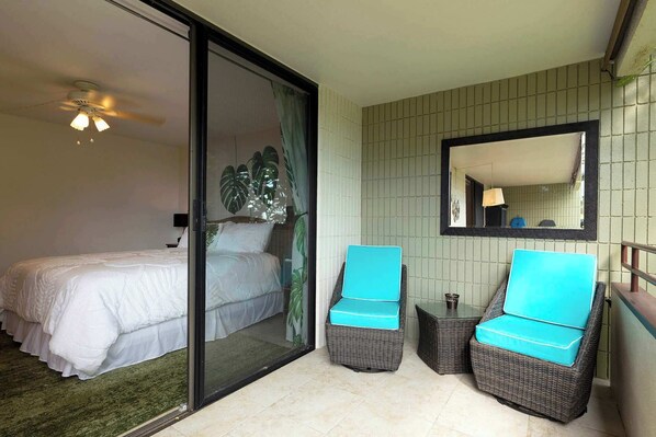Un dormitorio con una cama, un ventanal corredero que da a un balcón, dos sillones de mimbre con cojines azules y un espejo en la pared.