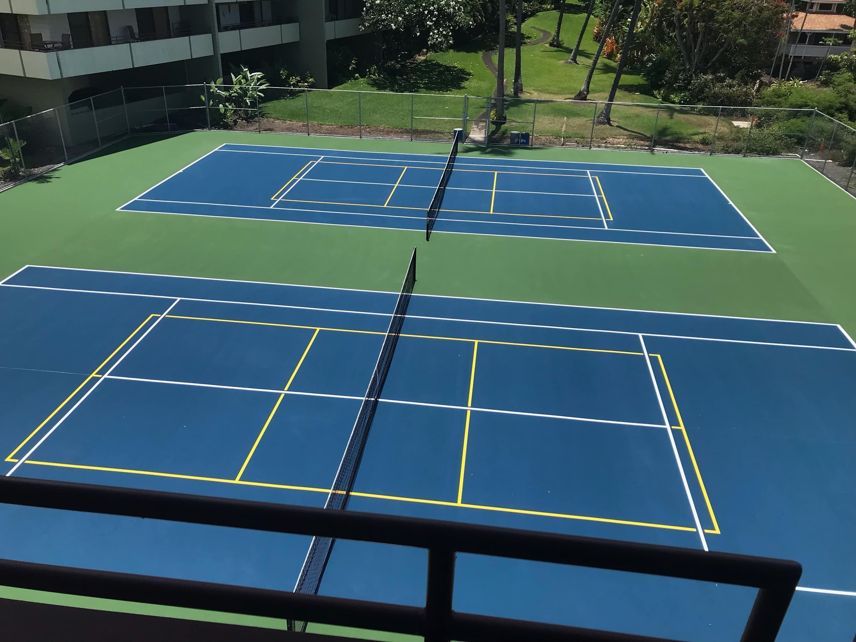 Tennisbaner omgivet af grøn vegetation og en bygning i baggrunden.
