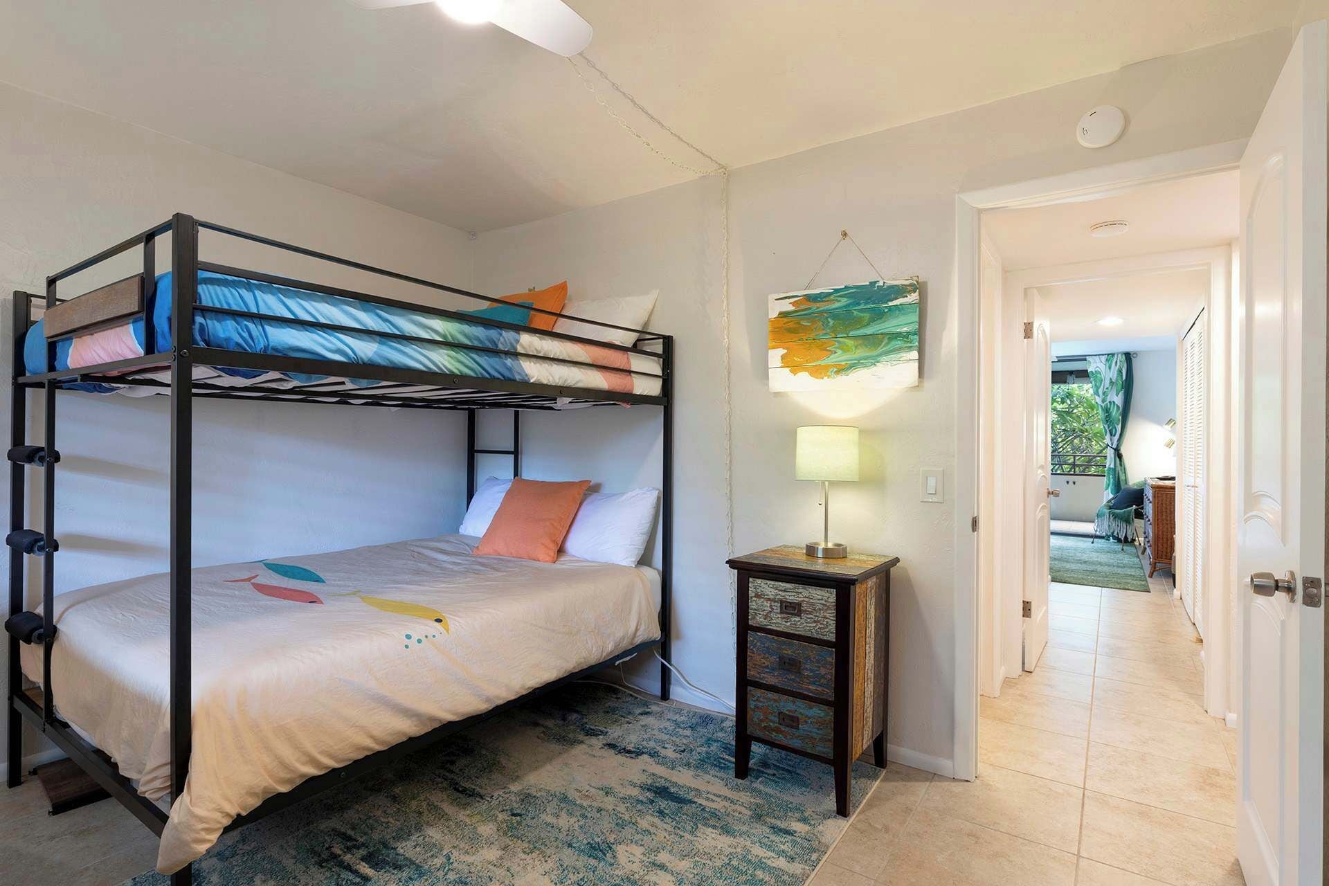 A bunk bed room with a small table and a lamp, a painting on the wall, and a door leading to a balcony.