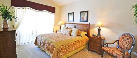 A bedroom with a bed, two bedside tables with lamps, a chair, a ceiling fan, and a large window with curtains.