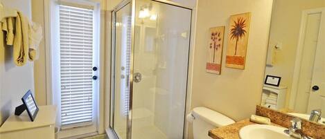 A bathroom with a glass-enclosed shower, a toilet, a sink, and a mirror.